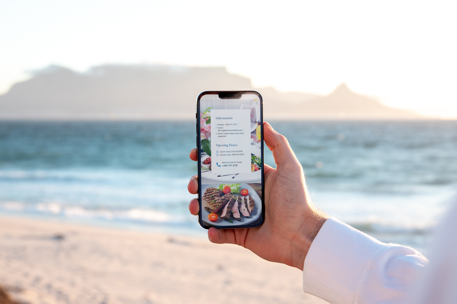 Holding phone on beach viewing Restaurant page on Hotel Anisette website